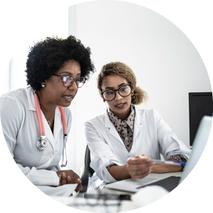 two female healthcare professionals sitting at a desk looking at a computer.