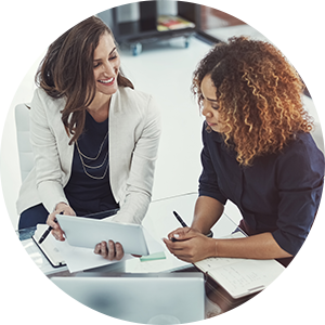 two women sitting at a desk looking at a paper and smiling